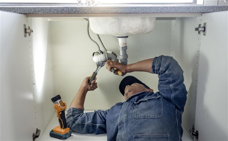 Plumber repairing pipes beneath a bathroom sink in Gibsonton