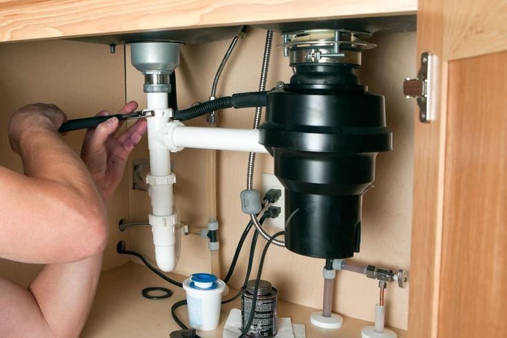 Plumber installing a garbage disposal beneath a kitchen sink in Gibsonton