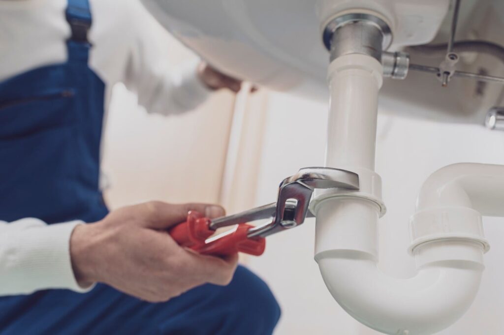 Plumber repairing a white drain pipe beneath a sink in Gibsonton