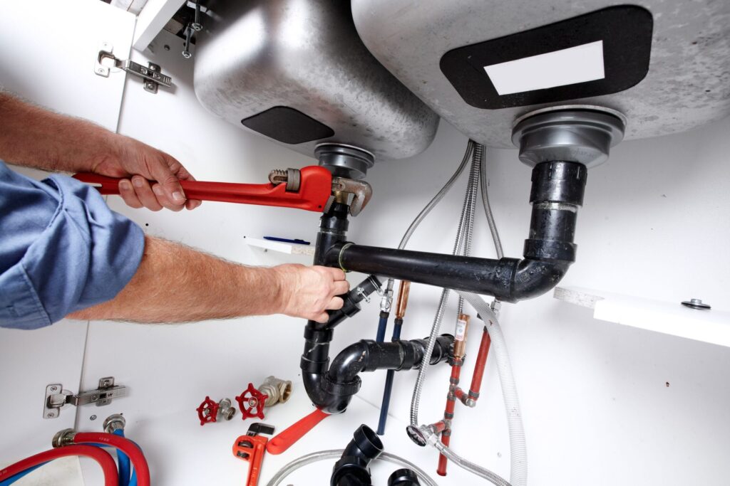 Plumber repairing drain pipes beneath a kitchen sink in Gibsonton